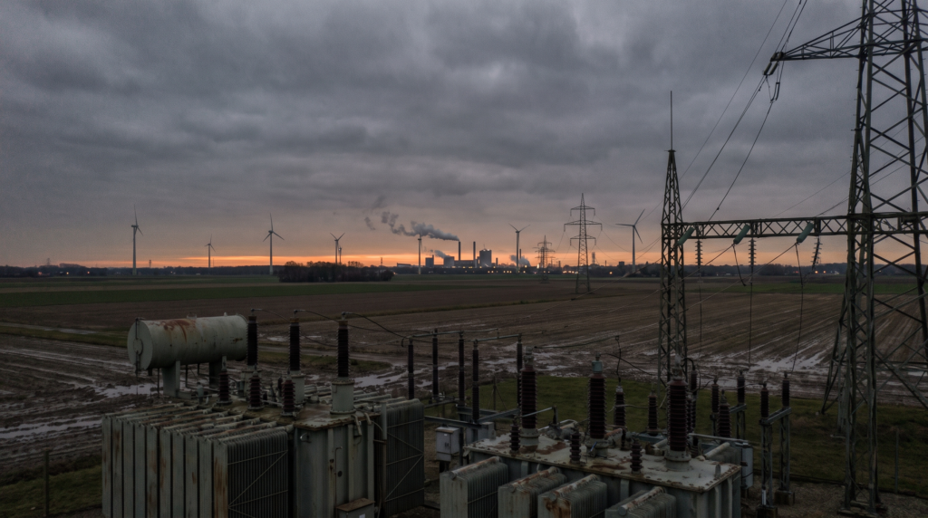 High-voltage substation and wind turbines at dusk on European farmland, representing energy as the base of sovereign compute
